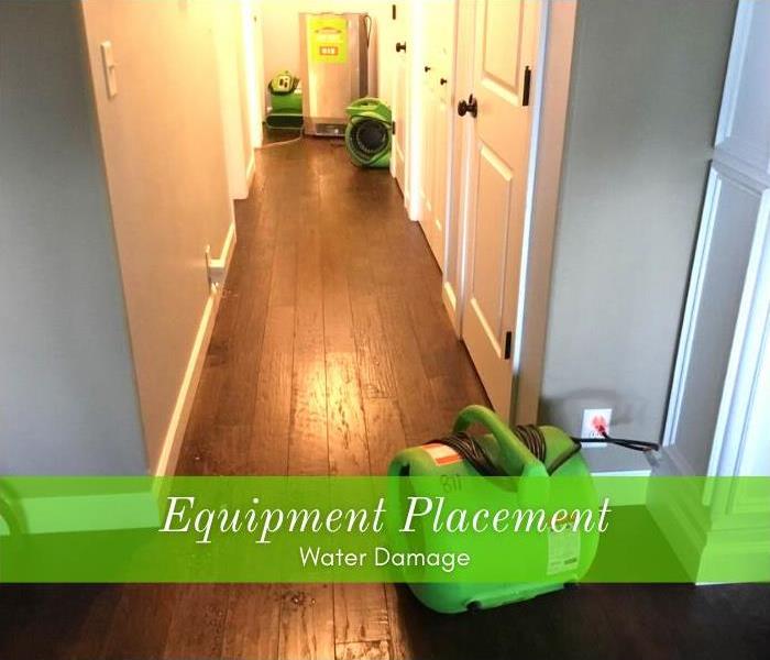 Dehumidifier and air movers placed to dry water damage in a hallway with wood flooring